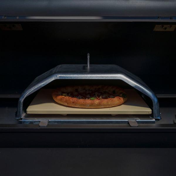 Wood-fired pizza cooking in Green Mountain Grills pizza attachment, featuring a stone base and protective cover.