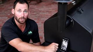 Man demonstrating GMG WiFi Grill features with smartphone, showcasing connectivity and grilling technology.