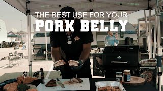 Man in a black shirt holding grilled pork belly in front of a grill under a tent, with text overlay "THE BEST USE FOR YOUR PORK BELLY," showcasing barbecue preparation, relevant to Green Mountain Grills and pork recipes.