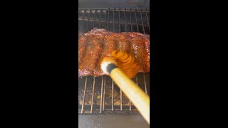 Smoked beef ribs being brushed with sauce on a pellet grill, showcasing grilling techniques for flavorful meat preparation.